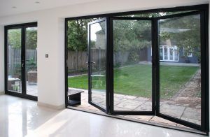black aluminium bifold doors, 3 pane half open with a glass view of the garden
